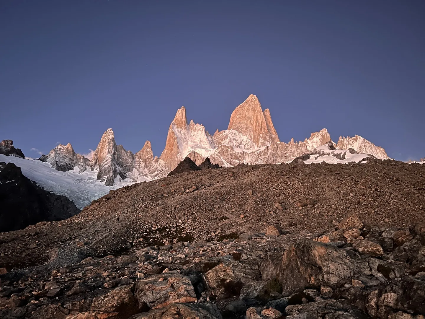First light turning the Fitz Roy spires pink above the rocky moraine near the top of the climb