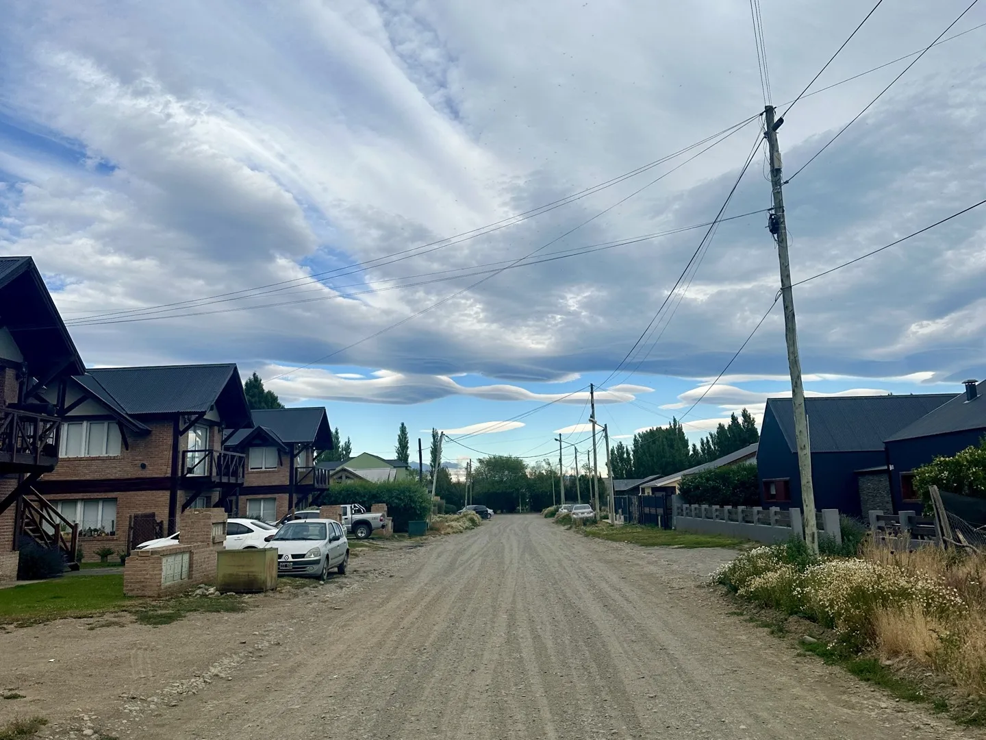 A gravel street of timber cabins in El Calafate under lenticular clouds in the morning