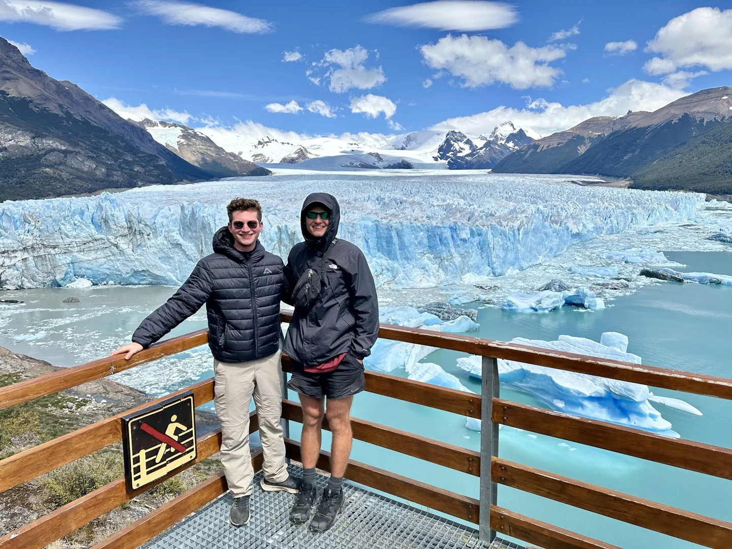 Two hikers at a boardwalk railing with the front of Perito Moreno Glacier behind them