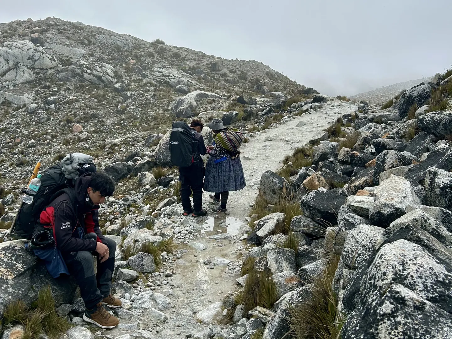 Climbers resting on the rocks by the trail to the glacier, a woman in traditional Bolivian dress on the path