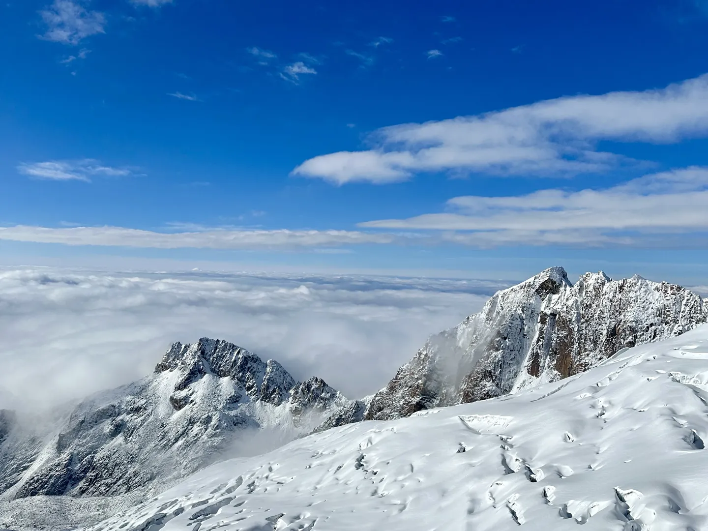 Rocky snow-covered peaks of the Cordillera Real rising out of the cloud on the way down