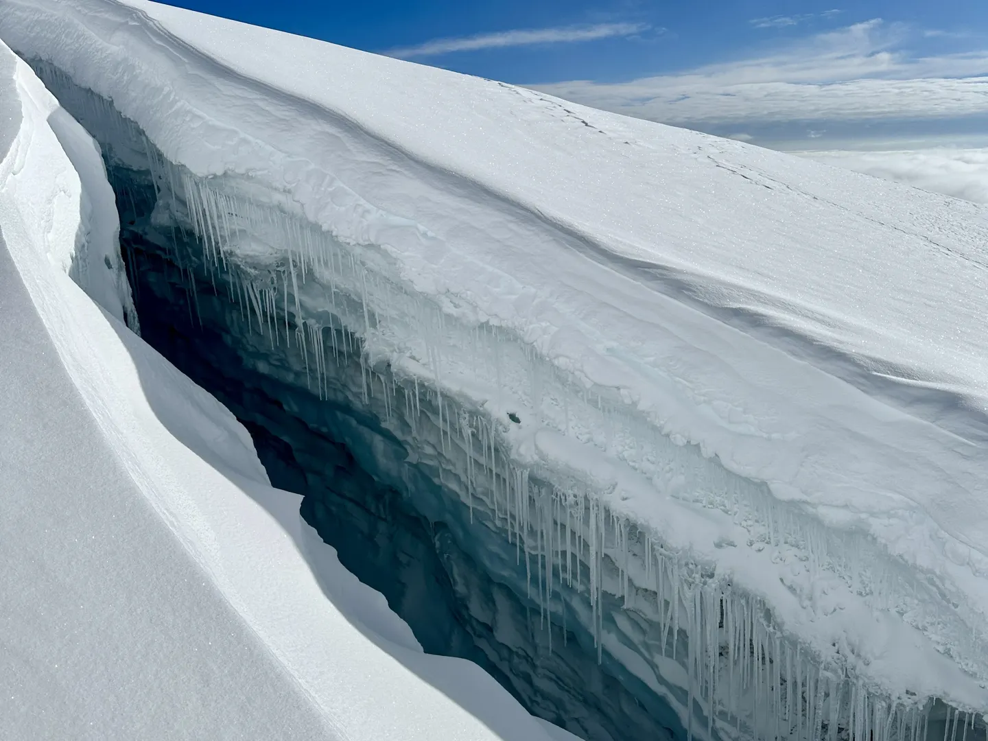A deep crevasse split through the glacier on Huayna Potosi, its blue walls hung with icicles