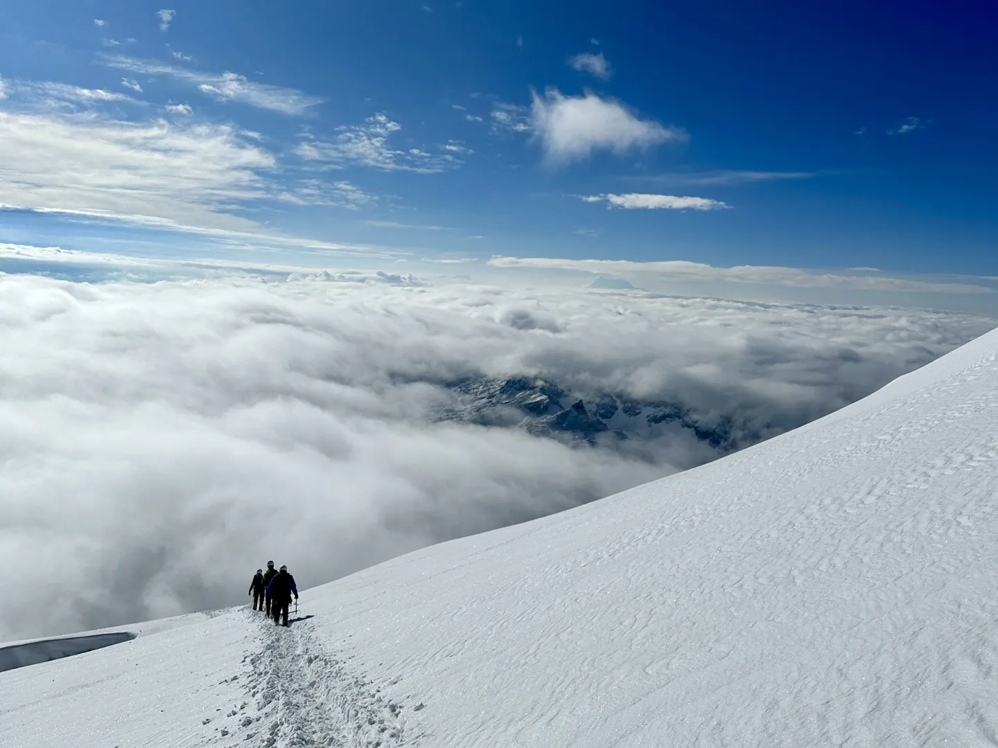 Three climbers on the wide snow slope high on Huayna Potosi above a thick sea of cloud