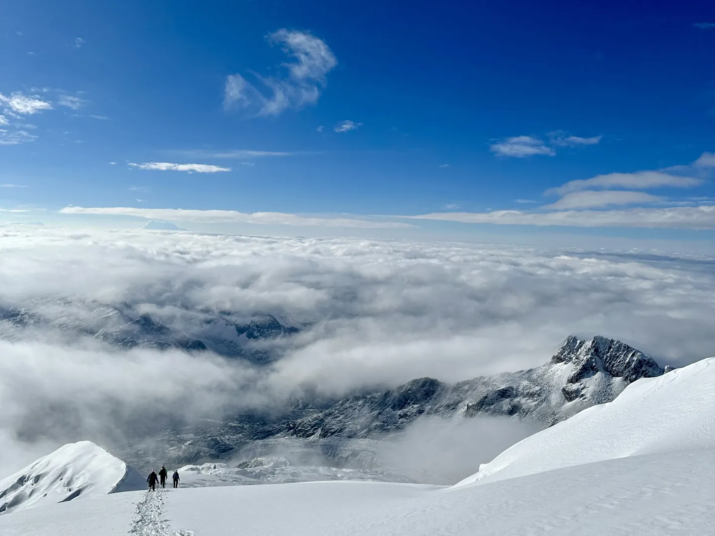 Three climbers descending the snow slope towards high camp above a thick sea of cloud