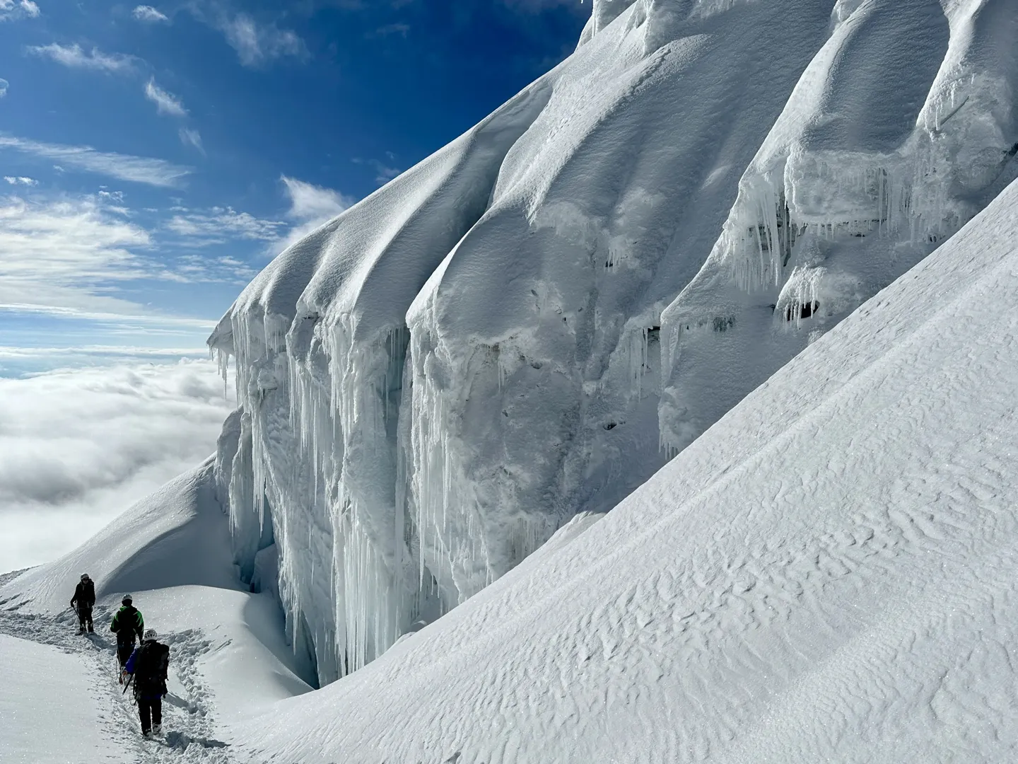 Climbers descending beneath a towering wall of blue seracs on Huayna Potosi, cloud far below