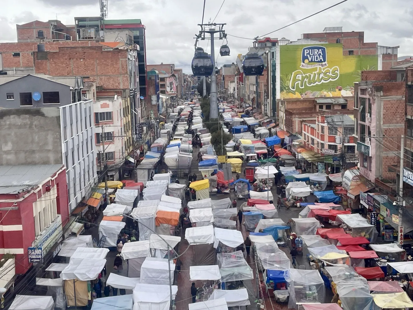 Cable cars passing above a La Paz street packed with market stall canopies