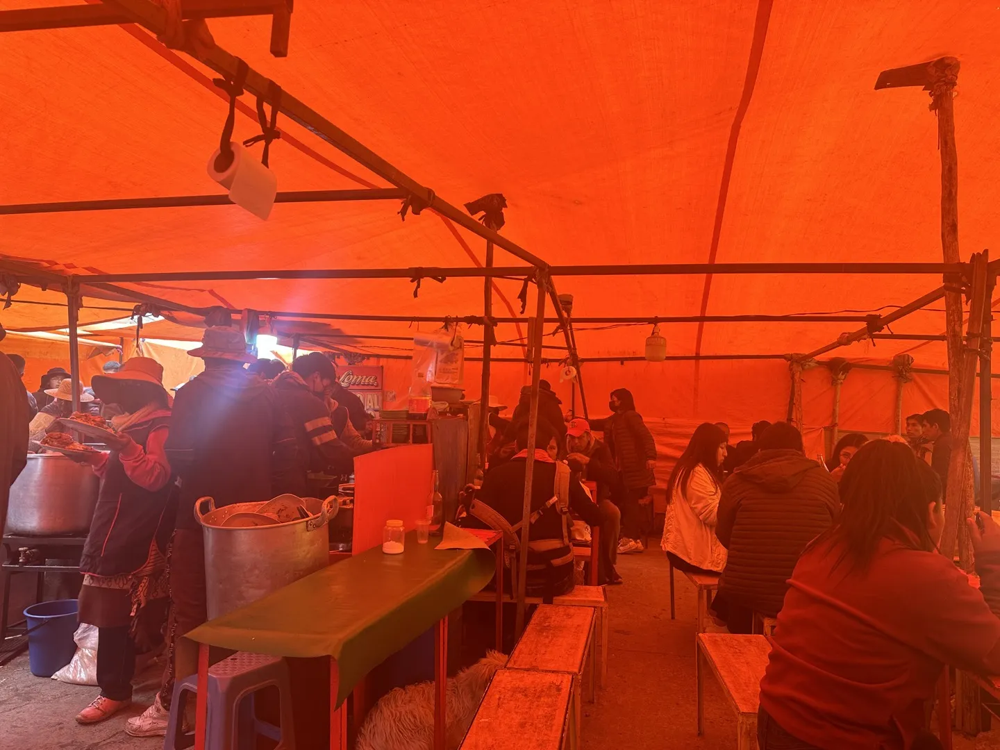 People eating at benches inside an orange tarpaulin food tent at a La Paz market