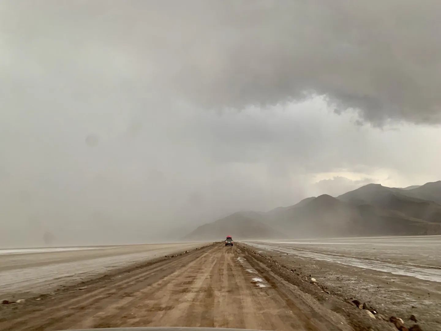 A tour 4WD driving through heavy rain on the track along the edge of the Salar towards Puerto Chuvica