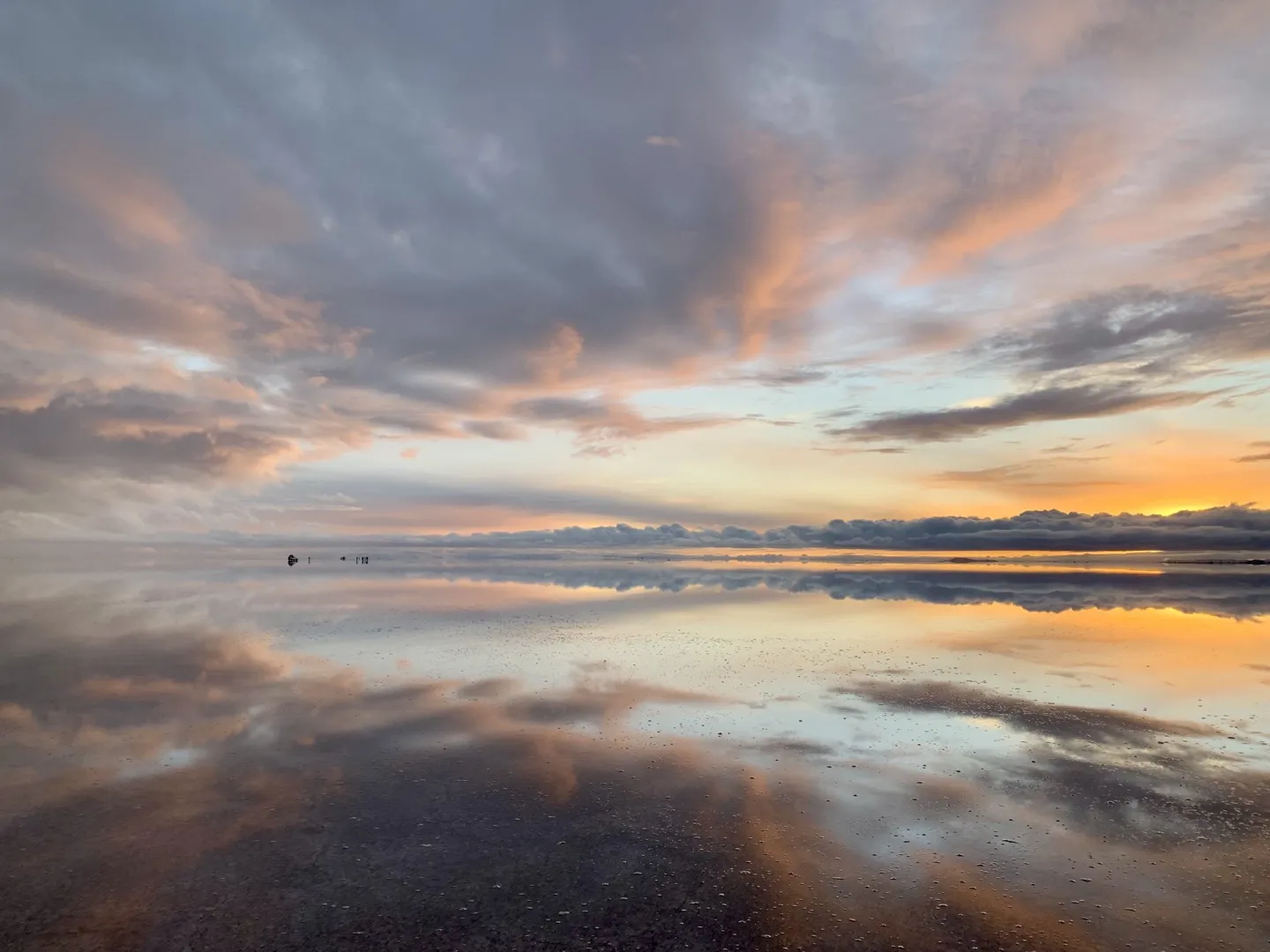Orange and pink sunrise reflected across the flooded Salar de Uyuni all the way to the horizon
