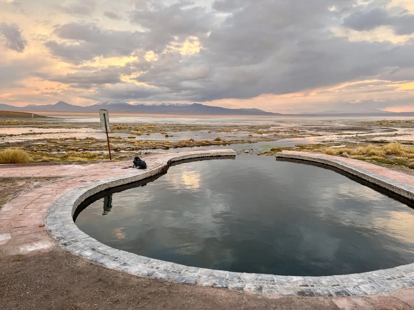 The stone-edged pool of the Polques hot springs at sunset, looking out over the Salar de Chalviri