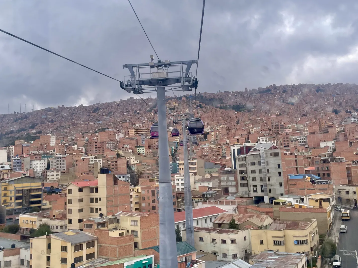 Cable car cabins crossing above the red-brick houses that climb the La Paz valley