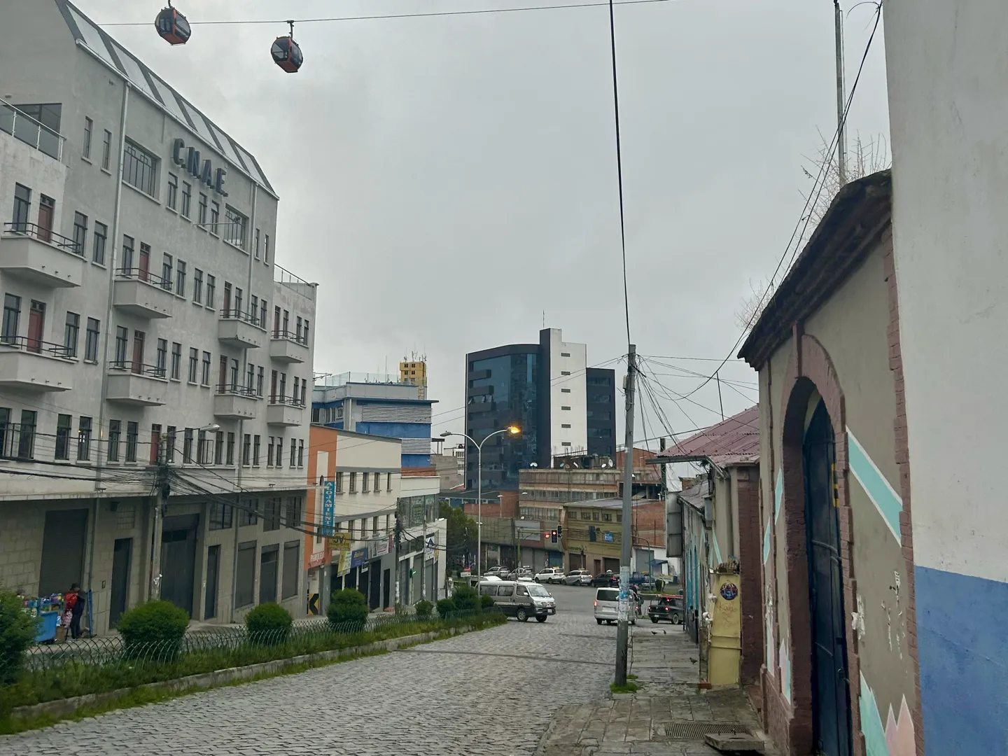 A quiet cobbled street in La Paz with cable cars crossing above the rooftops