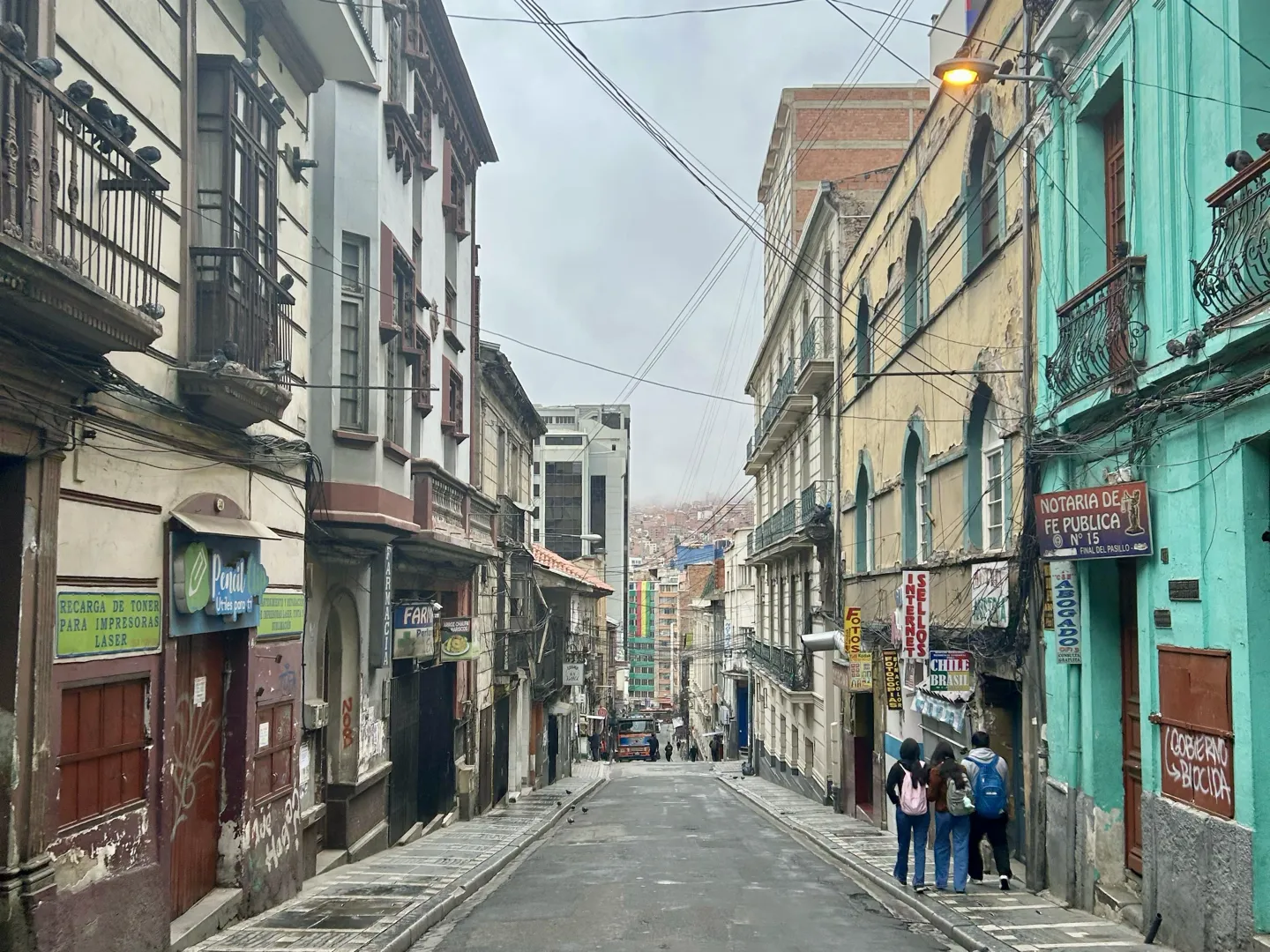 Backpackers walking down a steep colonial street in central La Paz with the valley slopes behind