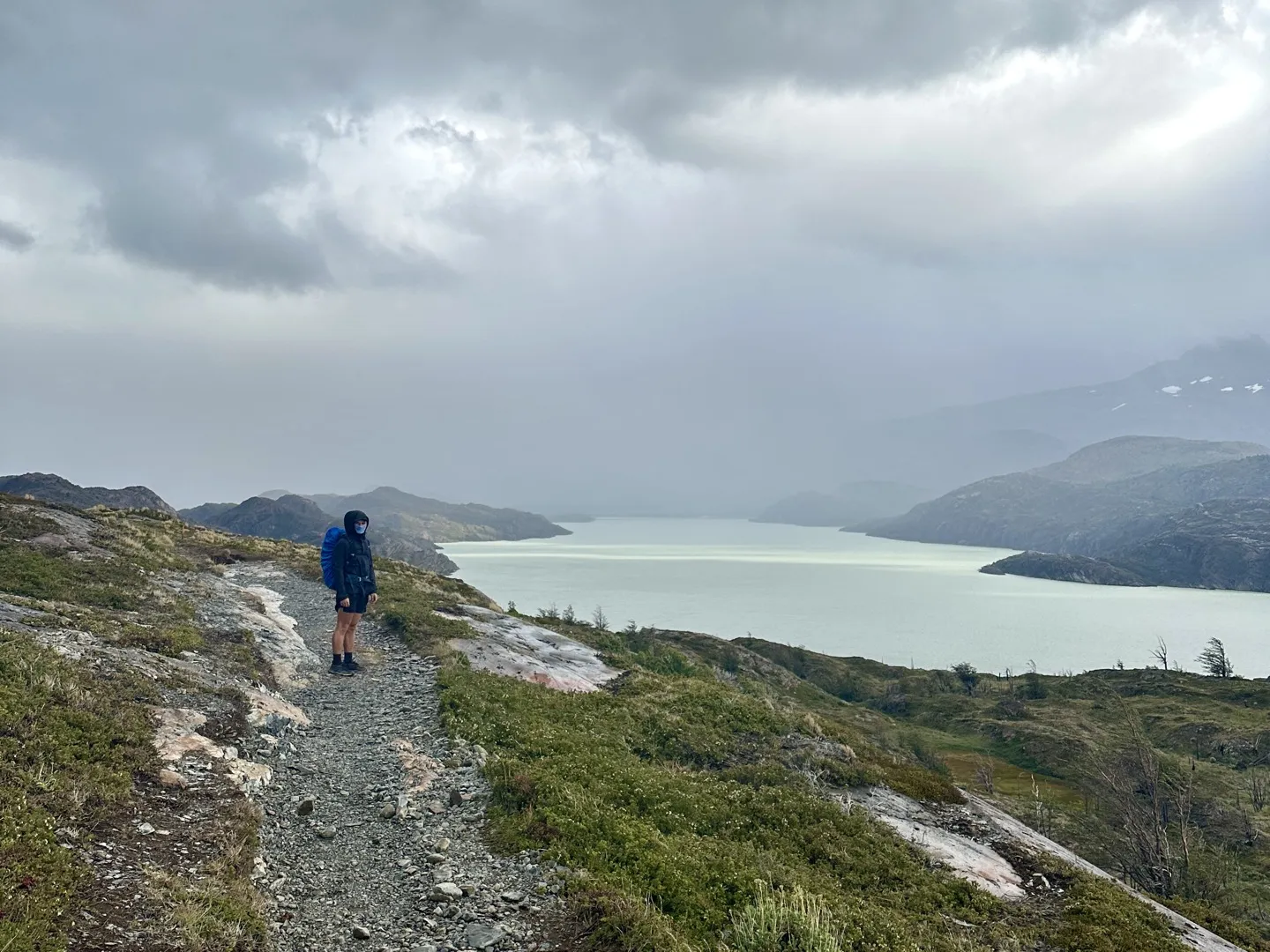 Hiker on the rocky trail to Grey Glacier, looking out over Lago Grey under low cloud
