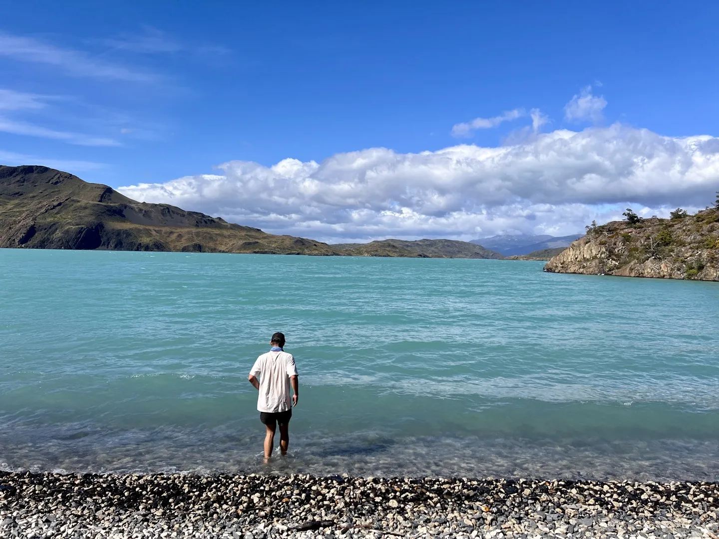 Hiker wading into Lago Nordenskjöld from a pebble beach on the trail to Chileno