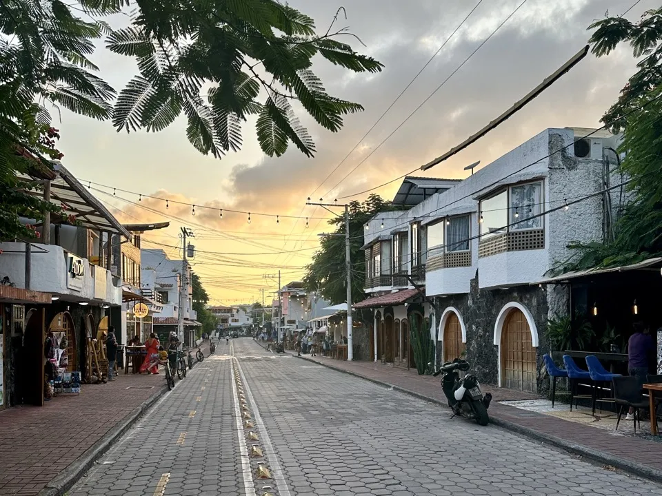 A street of shops and cafés on Santa Cruz at sunset, with a scooter parked by the kerb