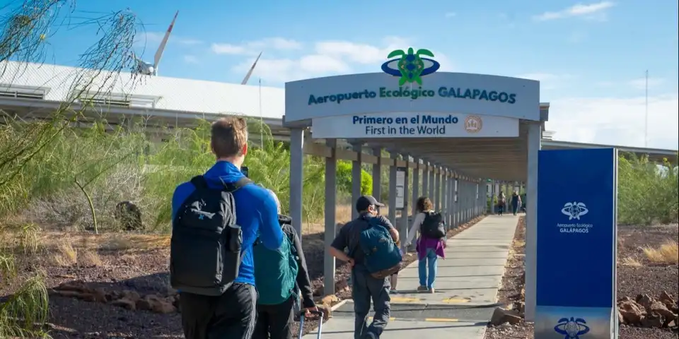Travellers with backpacks and a suitcase walking under the covered entrance to Seymour Airport on Baltra