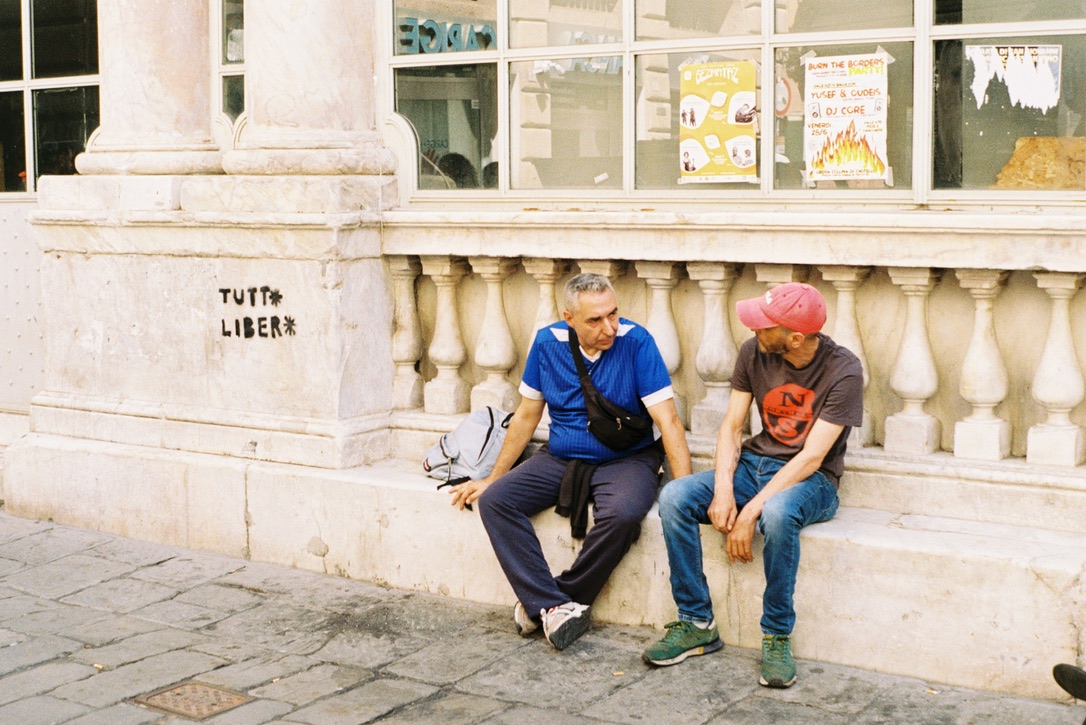 Two men in conversation outside a stone building