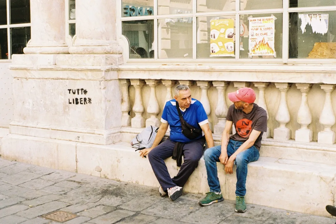 Two men in conversation outside a stone building