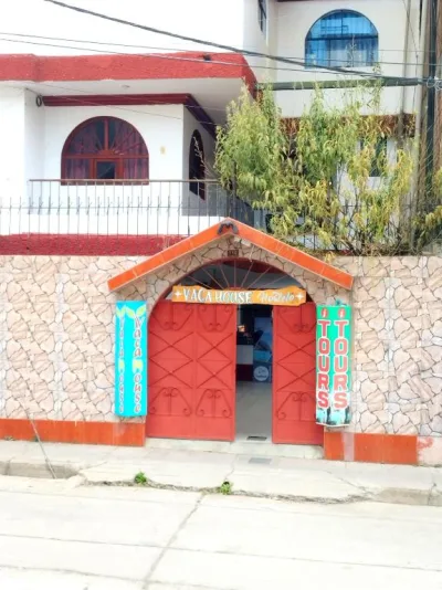 The red street entrance of Vaca House Hostel in Huaraz, with its stone facade and painted tour signs