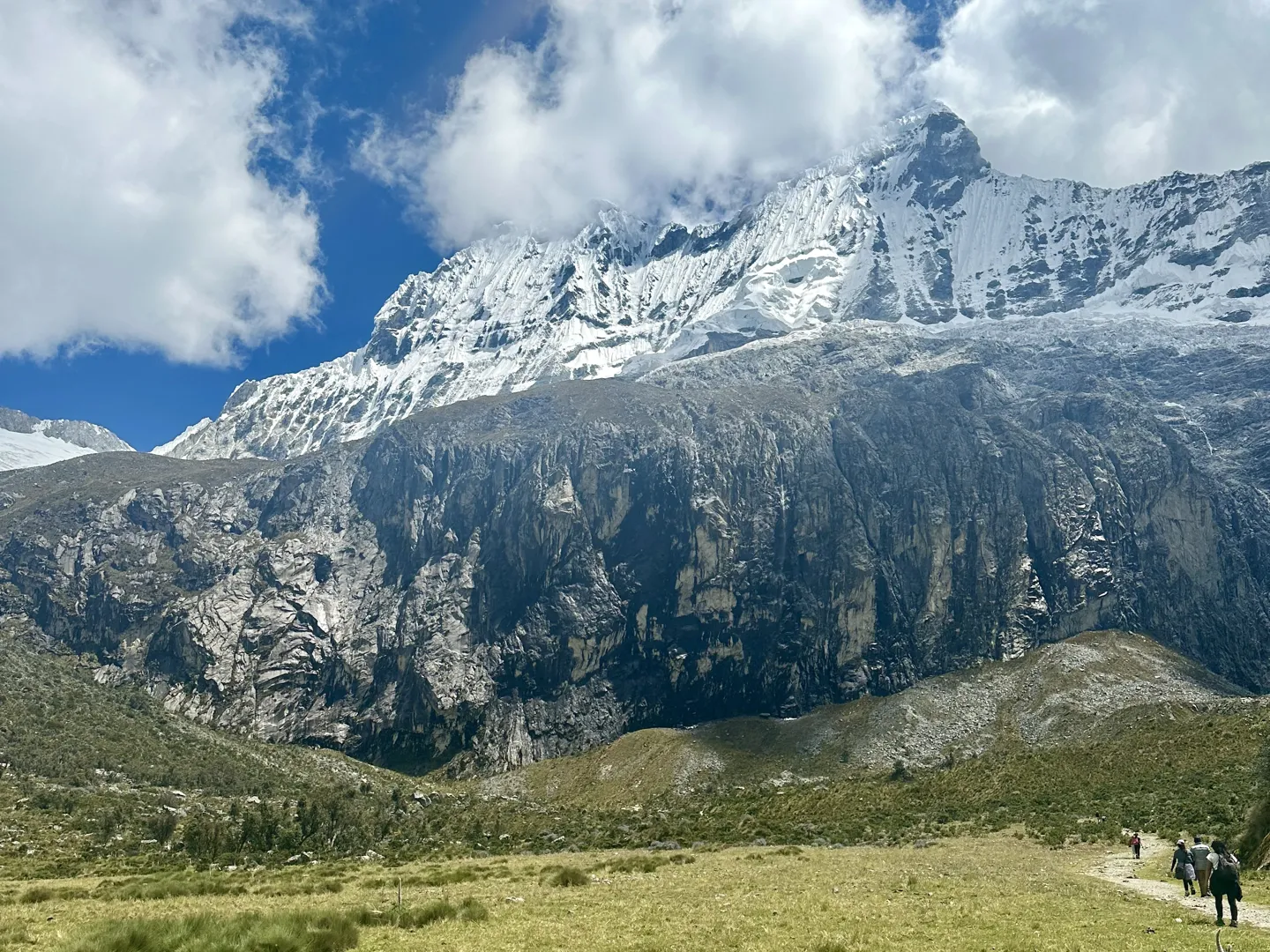 Hikers strung out along the Laguna 69 path beneath a huge snow-covered peak and dark rock cliffs