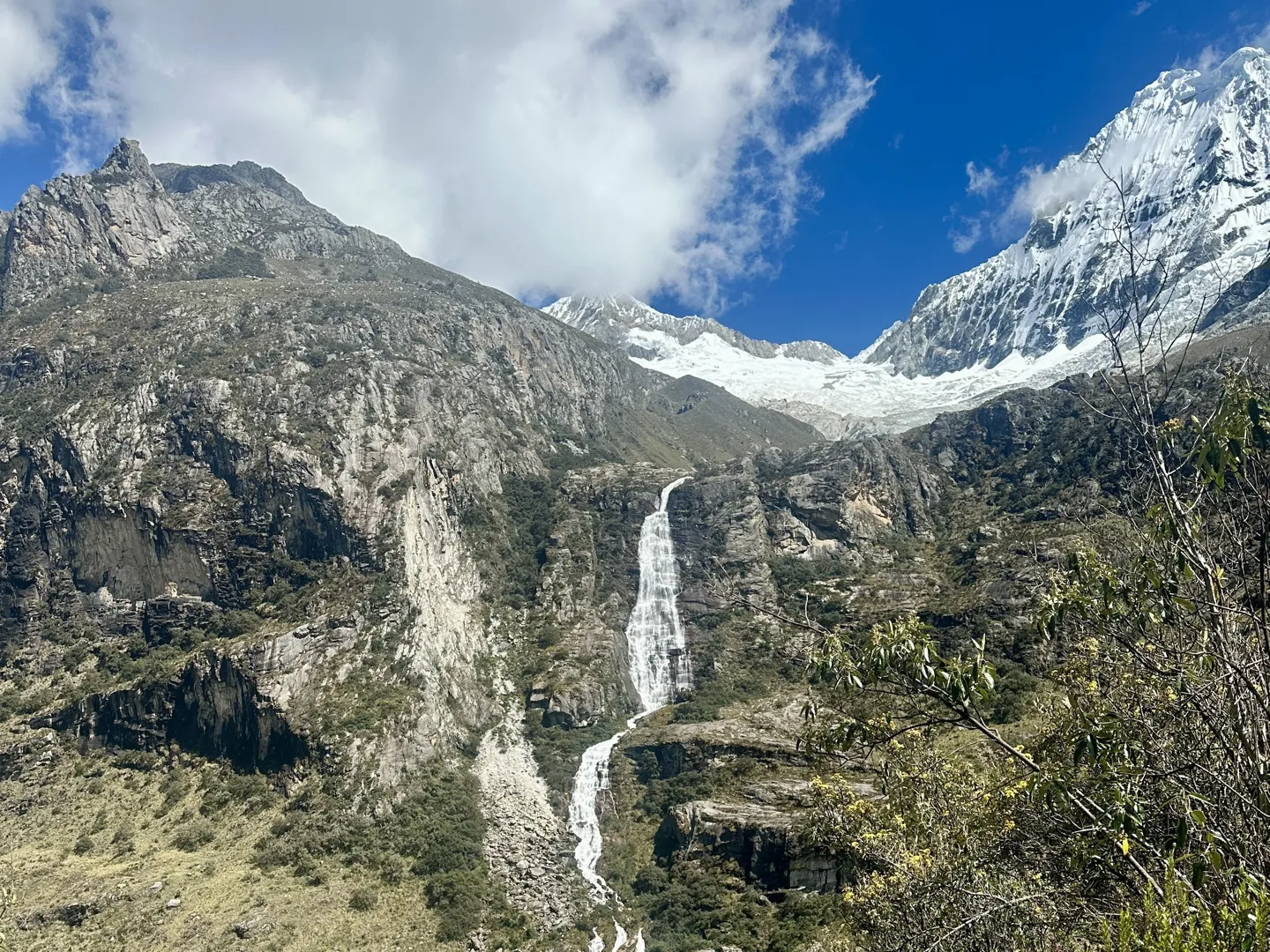 A waterfall dropping from the glacier high above the Laguna 69 trail, snow-covered peaks catching the light behind it