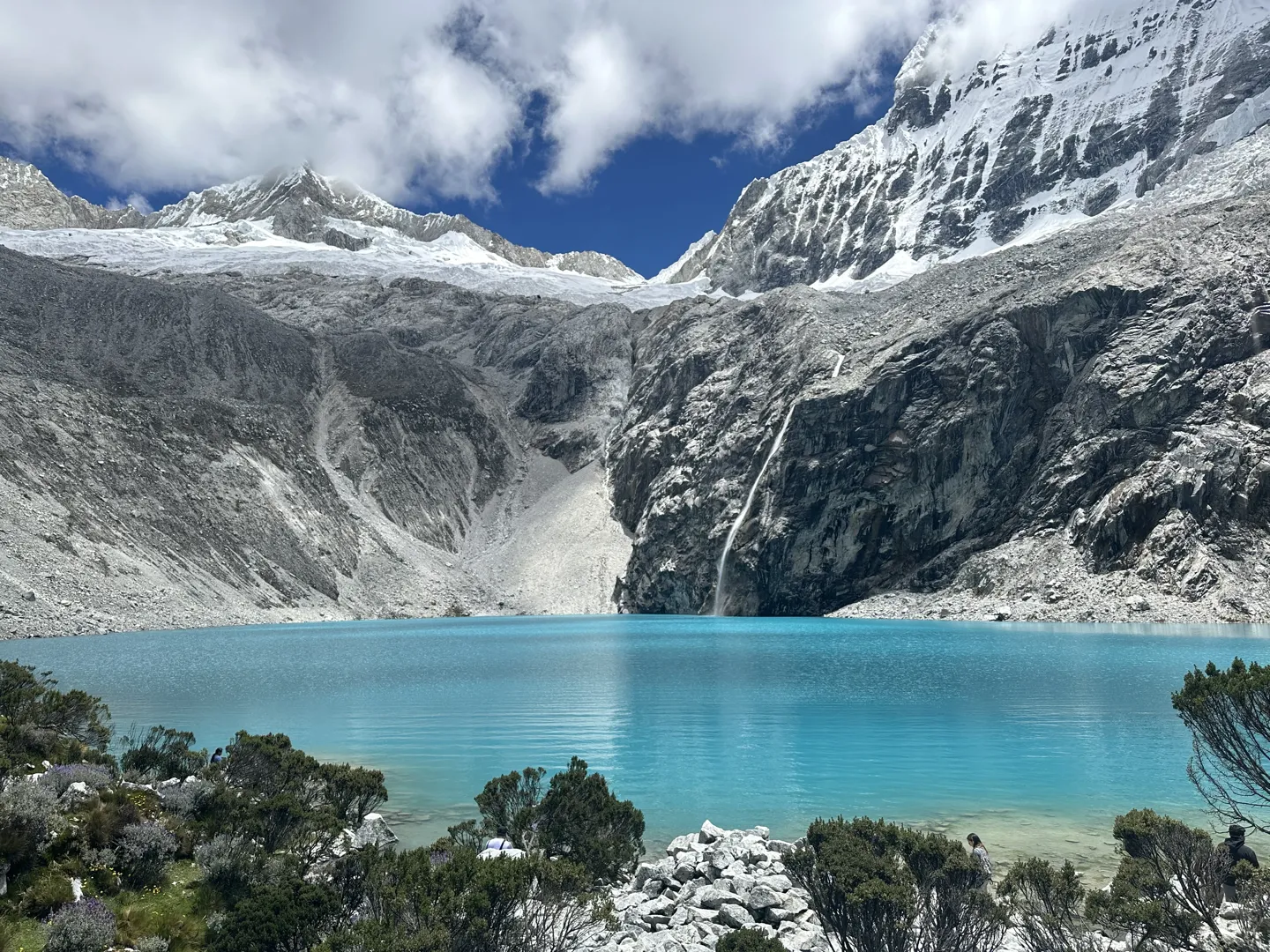 The bright turquoise water of Laguna 69 below a glacier, a waterfall running down the rock face into the lake