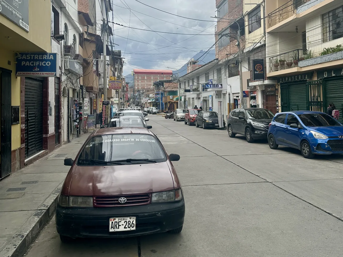 A street in central Huaraz lined with parked cars and shops, the Cordillera Blanca rising at the end of the road