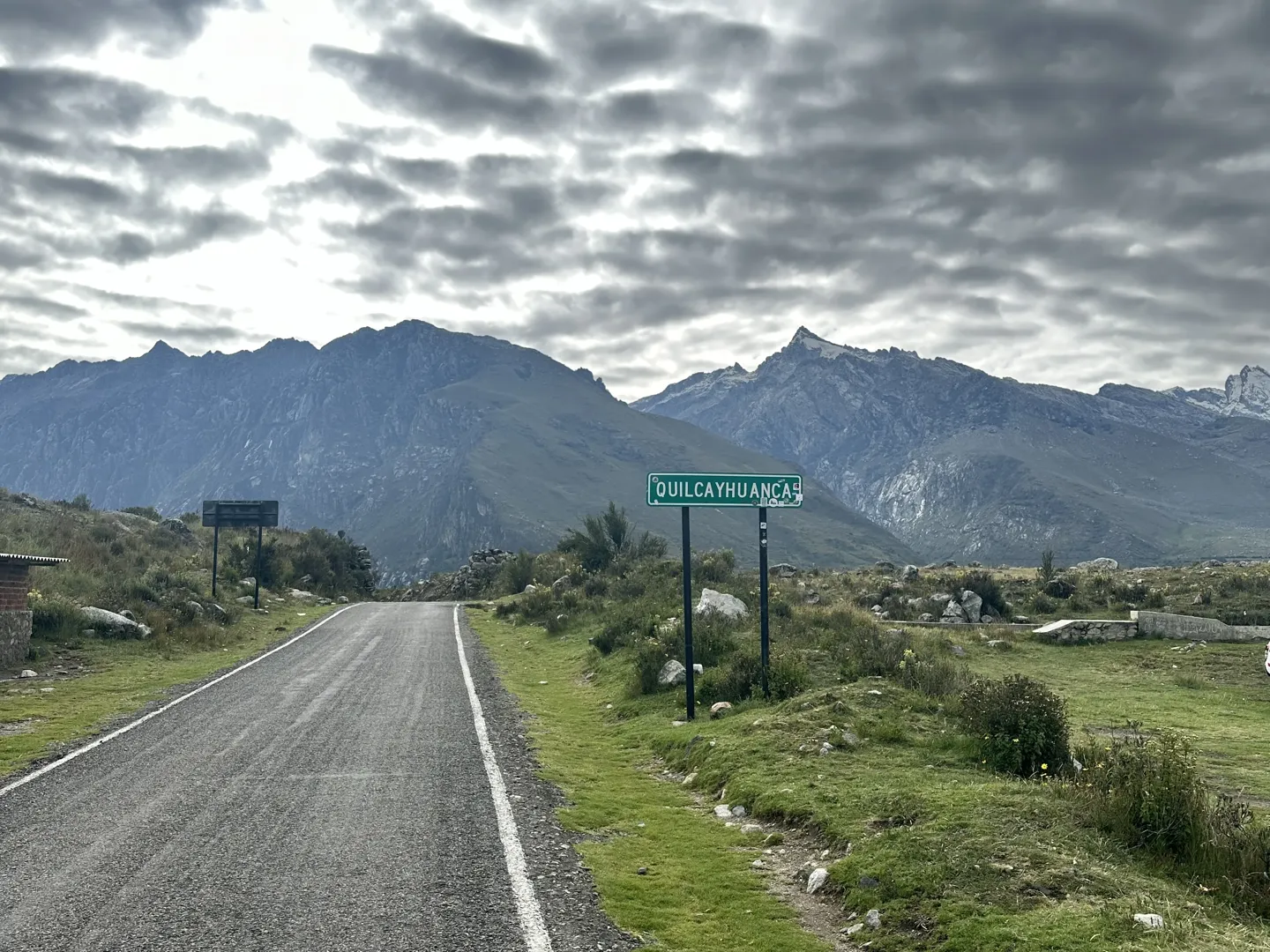 A road sign for Quilcayhuanca beside the paved road out of Huaraz, mountains under heavy cloud