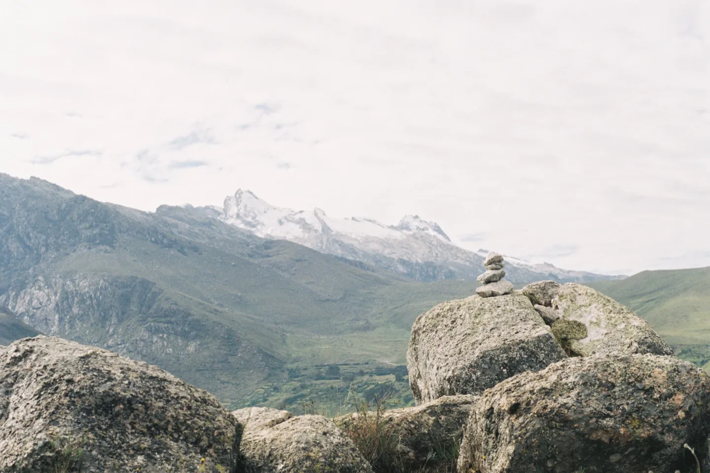 A small stone cairn on a boulder beside the Laguna Wilcacocha hike, a snow-capped Cordillera Blanca ridge behind