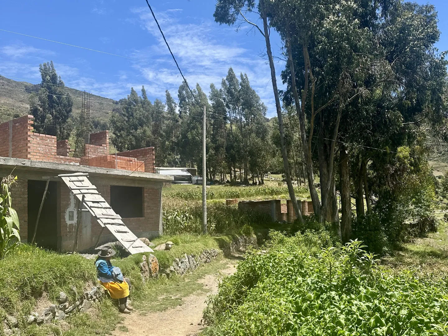 A brick house and dirt path in a small village on the Laguna Wilcacocha trail, a resident sitting outside