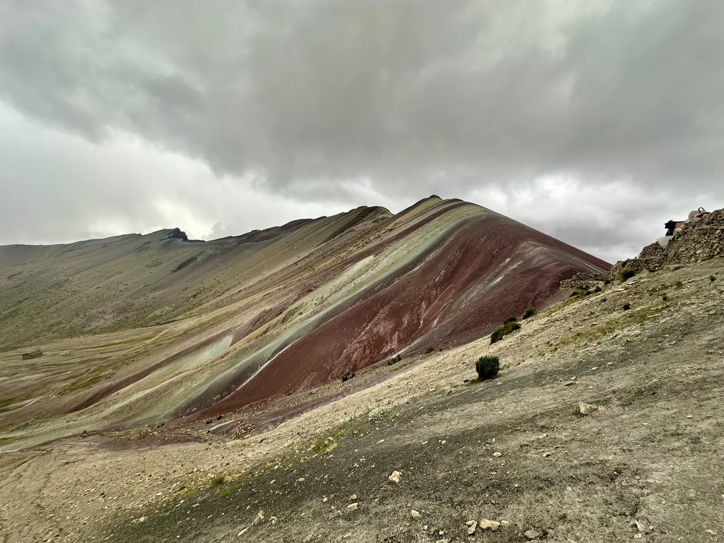 Rainbow Mountain's striped red and green slopes under a cloudy sky