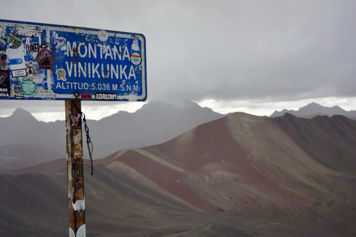 Sticker-covered summit sign reading Montaña Vinikunka, altitude 5,036 metres